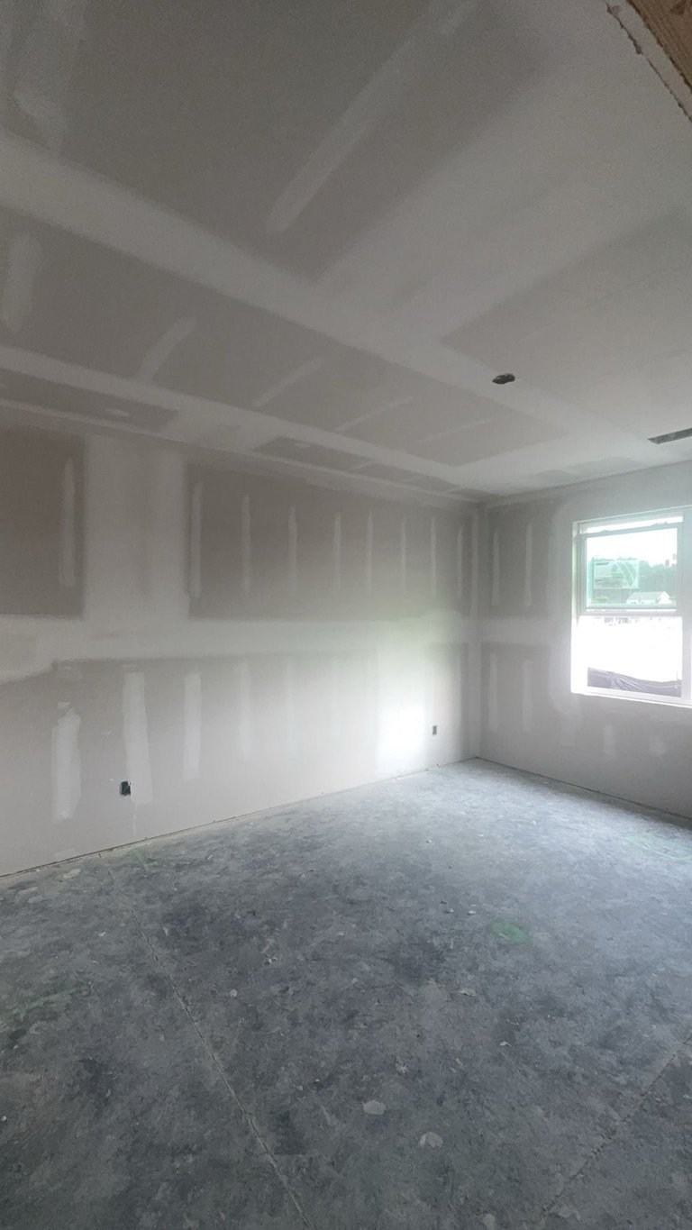 Empty room under construction with drywall walls, concrete floor, window, and recessed ceiling lights